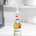 Hvit doseringspumpe på en Monin vaniljesirupflaske i glass, 70 cl.