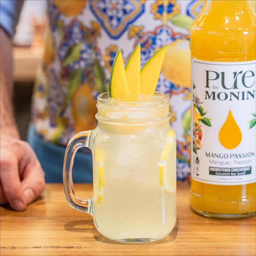 Pure by Monin Mango Passion konsentratflaske ved siden av en drink med mangoskiver.