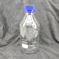 Klar 1000 ml borosilikatglass reagensflaske med blå skrukork og målemarkeringer.