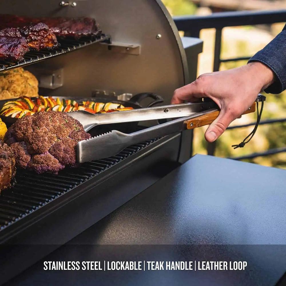 Traeger BBQ grilltang i rustfritt stål med teak-håndtak og lærhempe, brukt på en grill.
