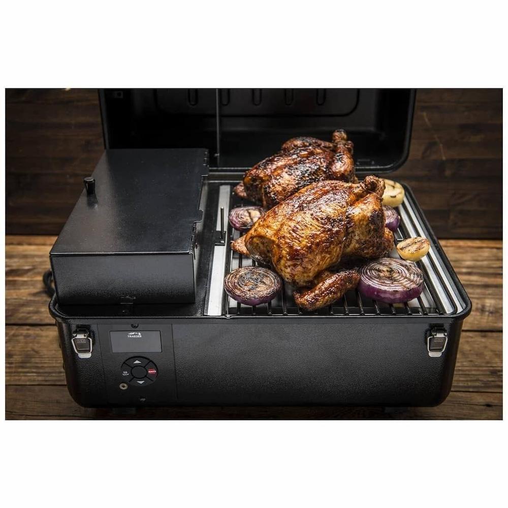 Traeger Ranger svart bærbar pelletsgrill med to hele kyllinger og løk på grillristen.