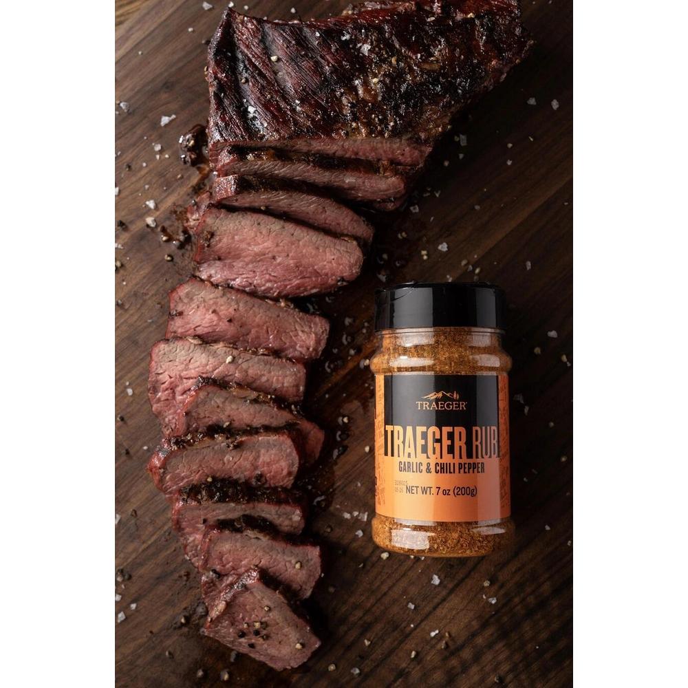 Traeger Rub Garlic & Chili Pepper 200g ved siden av skivet grillet kjøtt på et trebrett.