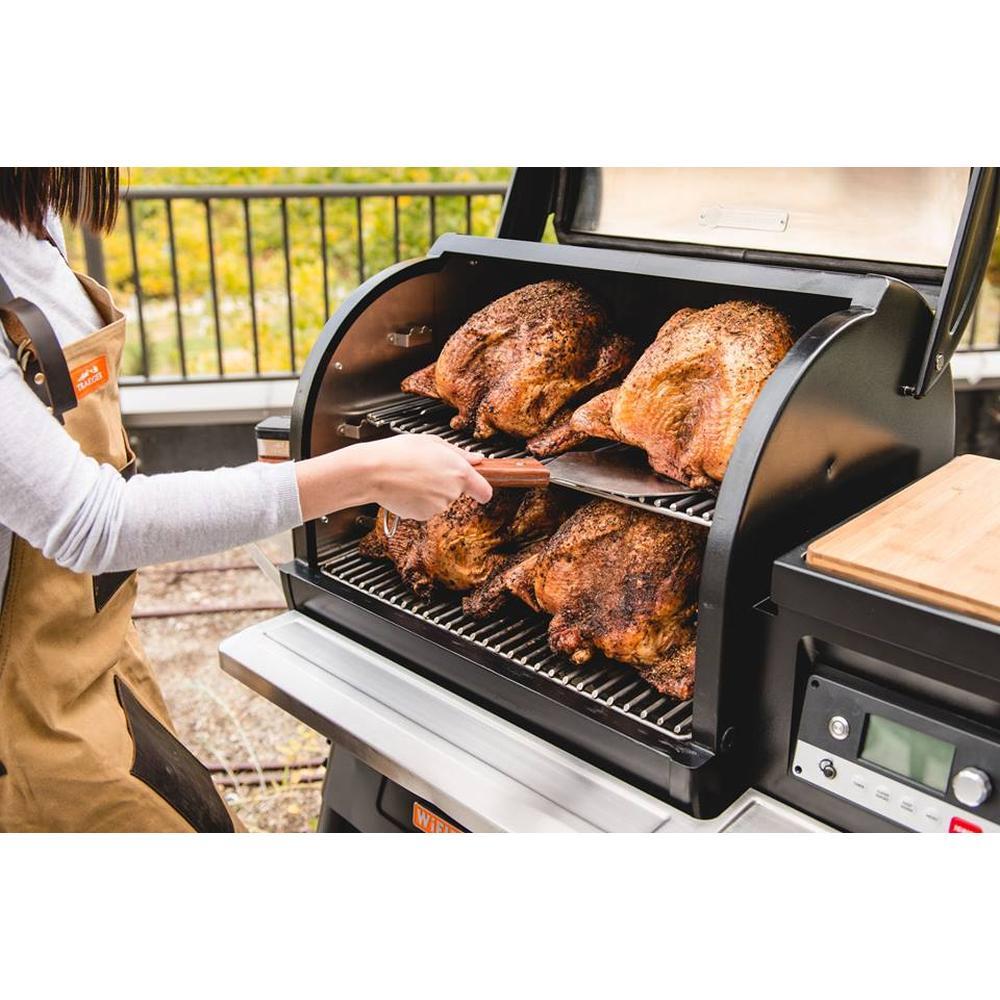 Kvinne bruker Traeger XXL BBQ Grillspade i rustfritt stål med trehåndtak til å snu kylling på en grill.